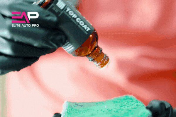 A gloved technician applies ceramic coating by dripping liquid from a brown bottle labeled "ION Top Coat" onto a green applicator pad, with the Elite Auto Pro logo in the corner. This close-up highlights the professional process of applying ceramic coating for vehicle surface protection.