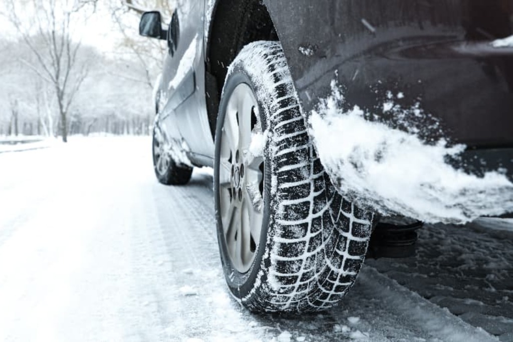 Close-up of a vehicle tire driving through snow on a Colorado Springs road, with slush and abrasive particles like salt and gravel clinging to the wheel well. This illustrates the constant exposure vehicles face during winter driving conditions.