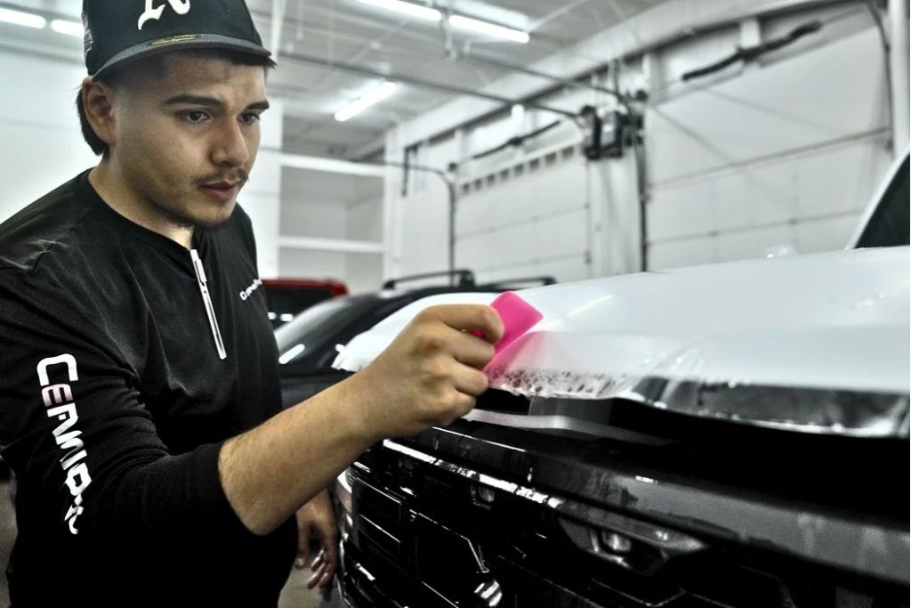 Technician using a squeegee tool to carefully apply paint protection film on a vehicle hood, demonstrating the importance of professional installation quality for long-lasting results.