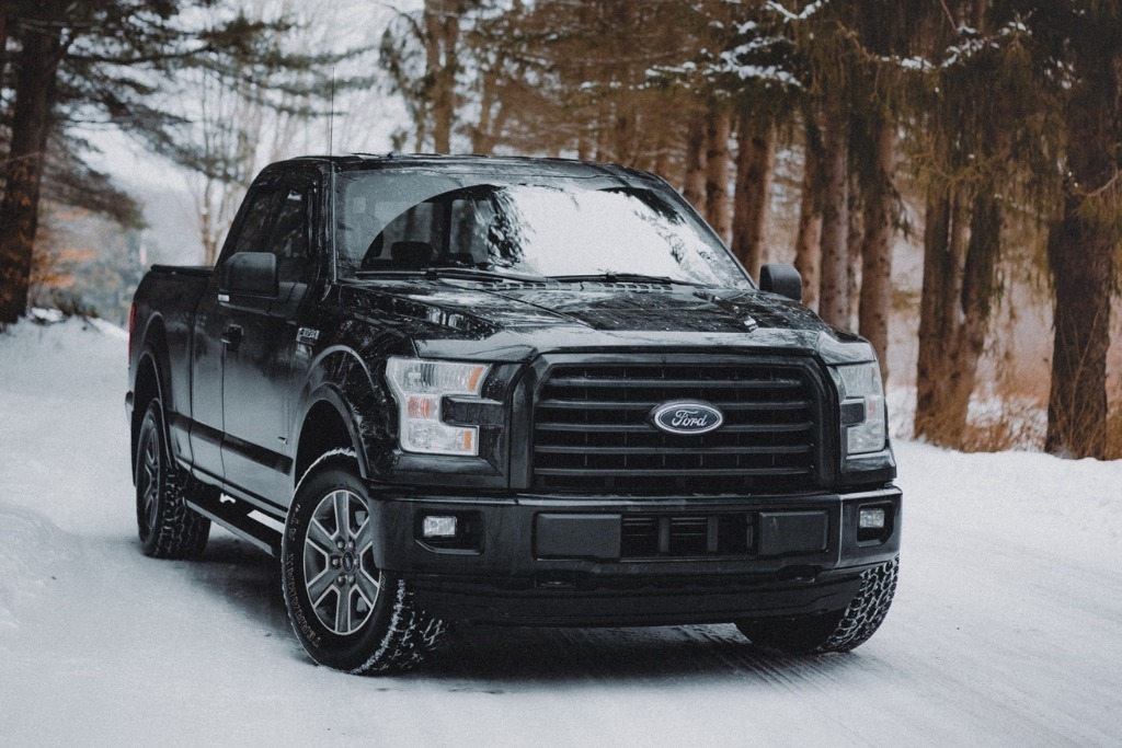 Black pickup truck parked on a snowy road surrounded by trees, illustrating Colorado Springs' unique climate challenges like snow, road salt, and seasonal stress that impact paint protection film.