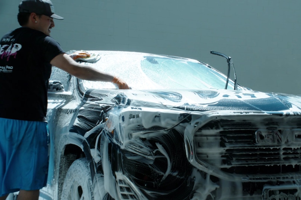 Man hand washing a GMC vehicle covered in soap suds, demonstrating proper maintenance habits to extend the lifespan of paint protection film.
