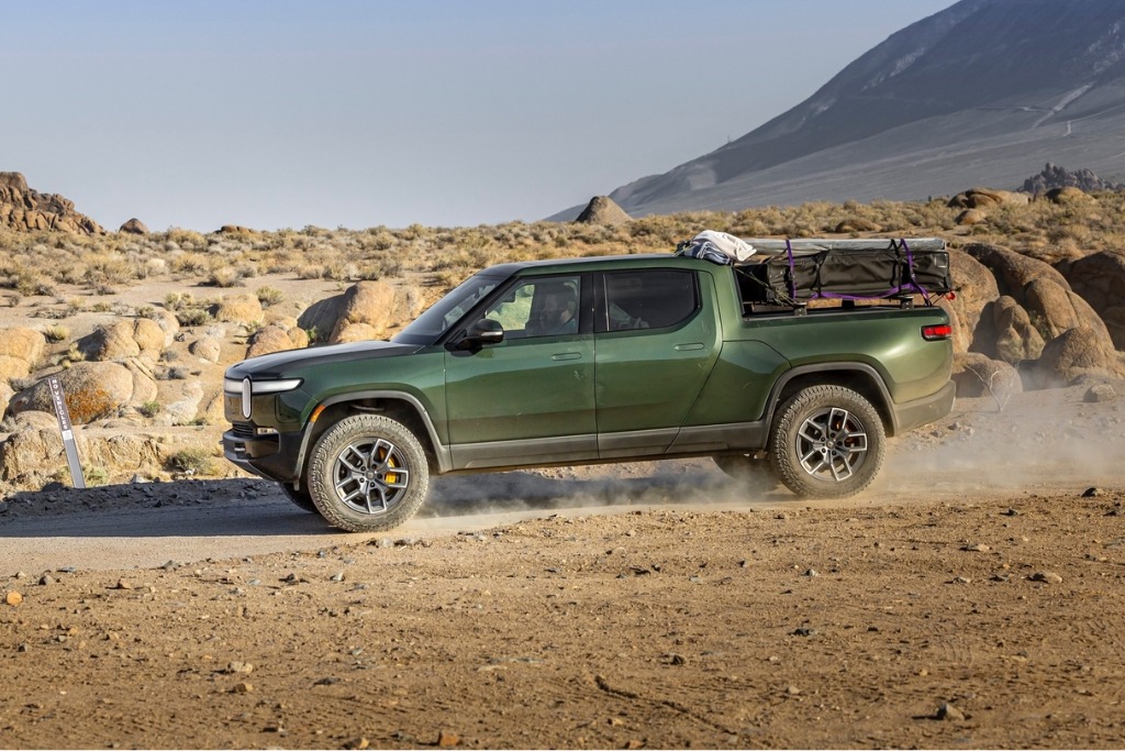 Green pickup truck driving on a dusty desert road with camping gear in the bed, showing how usage and driving conditions like off-roading affect paint protection film durability.