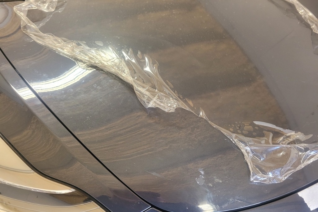 Close-up of worn paint protection film peeling off a car hood, showing damage and discoloration that signal it’s time to replace or reapply PPF.