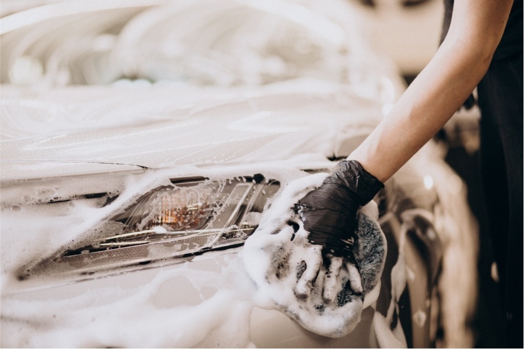 Close-up of a gloved hand washing a soapy car headlight with a sponge, showing proper care techniques as part of tips to maximize your PPF's lifespan.