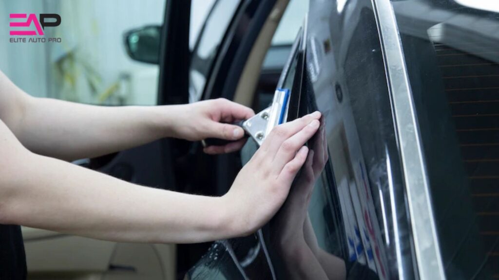 Technician uses a professional tool to apply window tint to a side window of a black car. The Elite Auto Pro logo is visible in the corner.