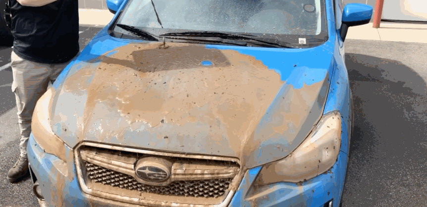 A blue Subaru partially covered in dried mud shows how ceramic coating causes the mud to easily rinse off, leaving clean paint underneath.