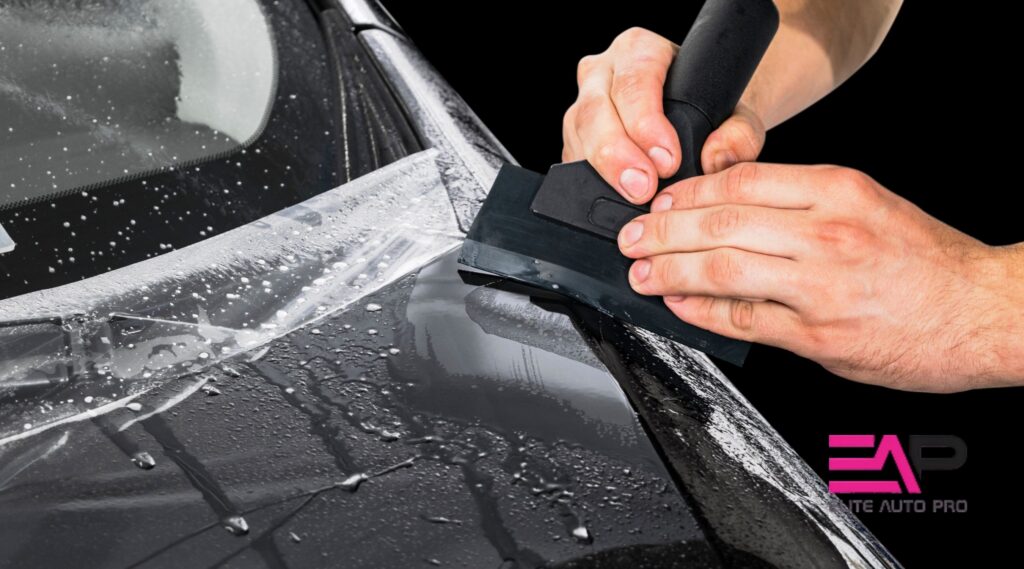 Technician installing paint protection film on a black car hood using a squeegee at Elite Auto PRO in Colorado Springs.