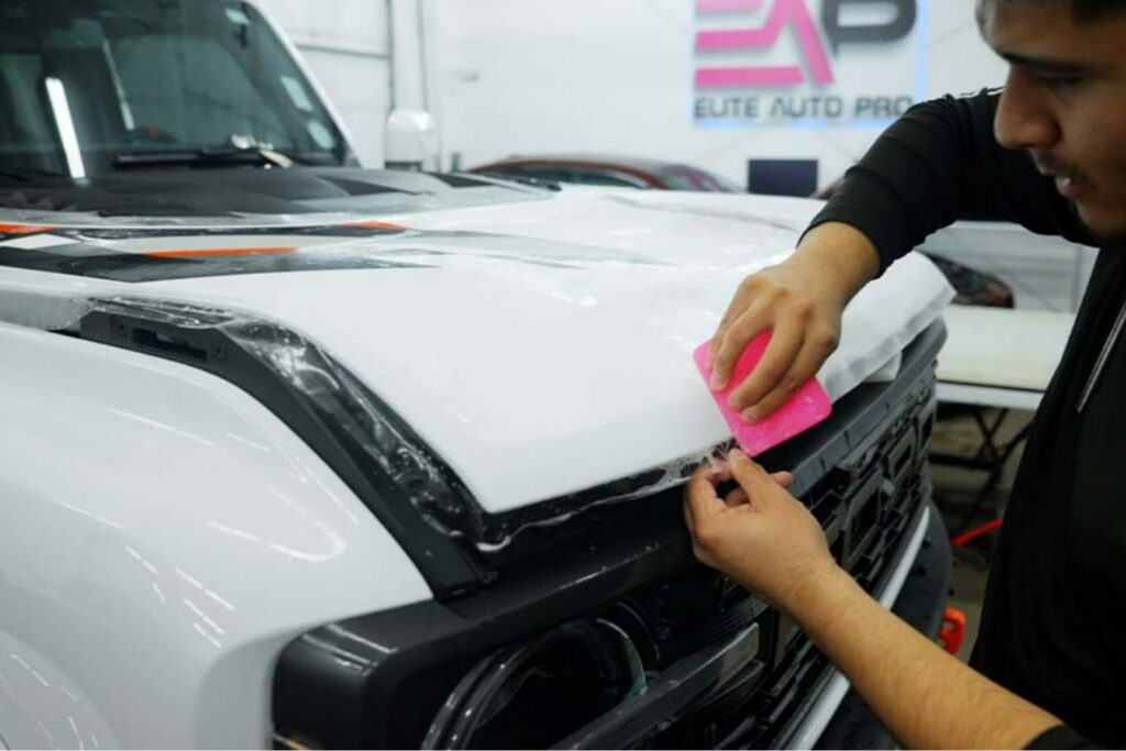 Professional installation of self-healing paint protection film on a vehicle's hood, showcasing a technician applying the film with a squeegee at Elite Auto Pro in Colorado Springs.