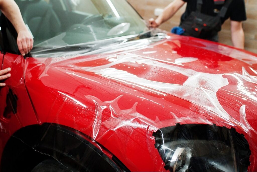 Professional installation of self-healing paint protection film on a red vehicle's hood, showcasing protective application against rock chips and UV damage.