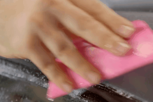 Hand applying a pink sponge to a vehicle surface, illustrating the process of detailing and maintaining paint protection film for optimal durability and appearance.