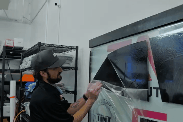 Technician applying window tint film to a red car door inside Elite Auto PRO shop